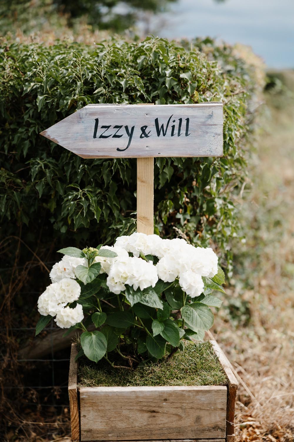 Wooden boxes labeled Izzy & Will with white flowers and greenery in handcrafted planters.
