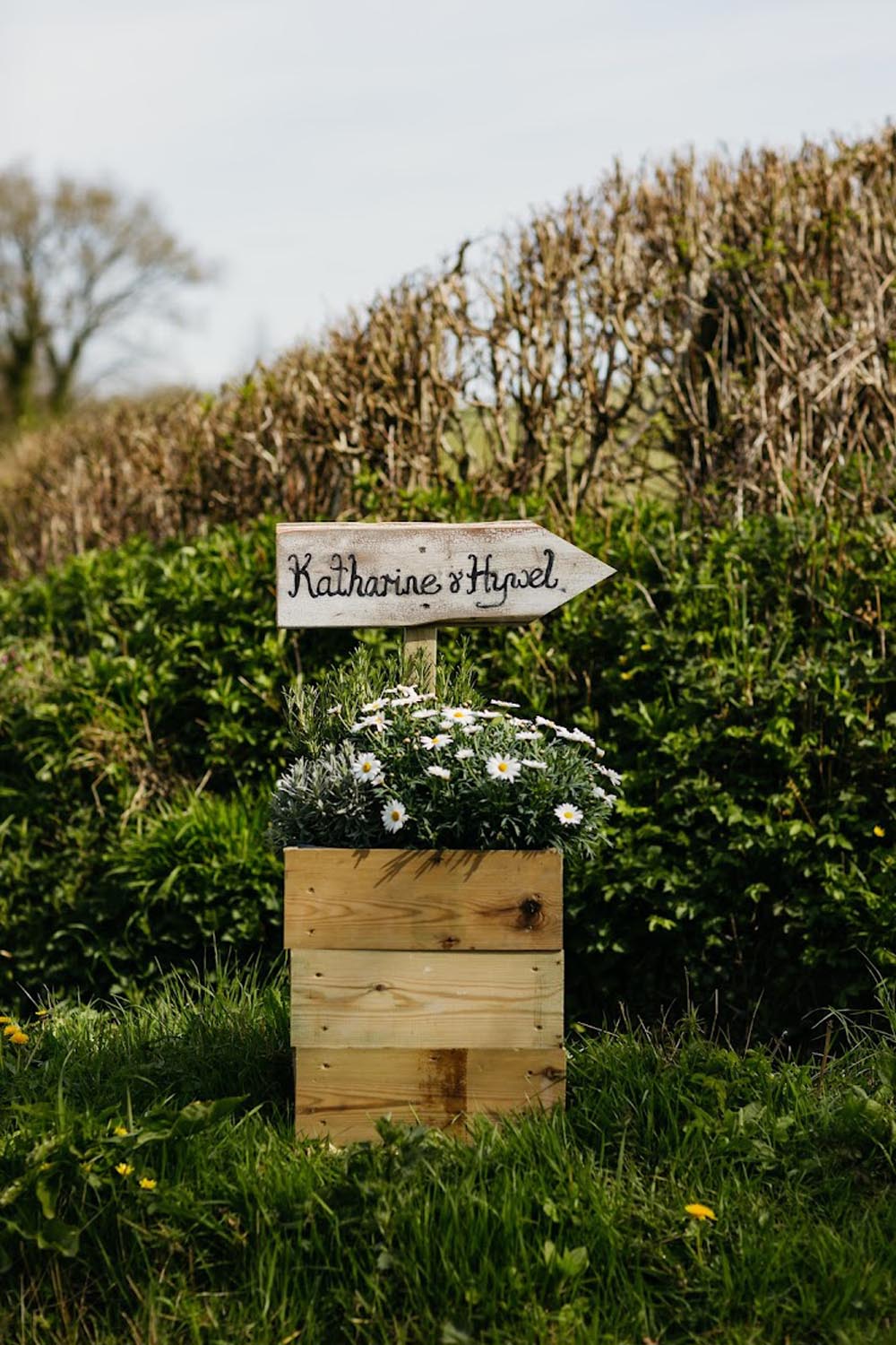 Wooden box featuring white flowers and a Katharines Hovel sign displayed on grass.